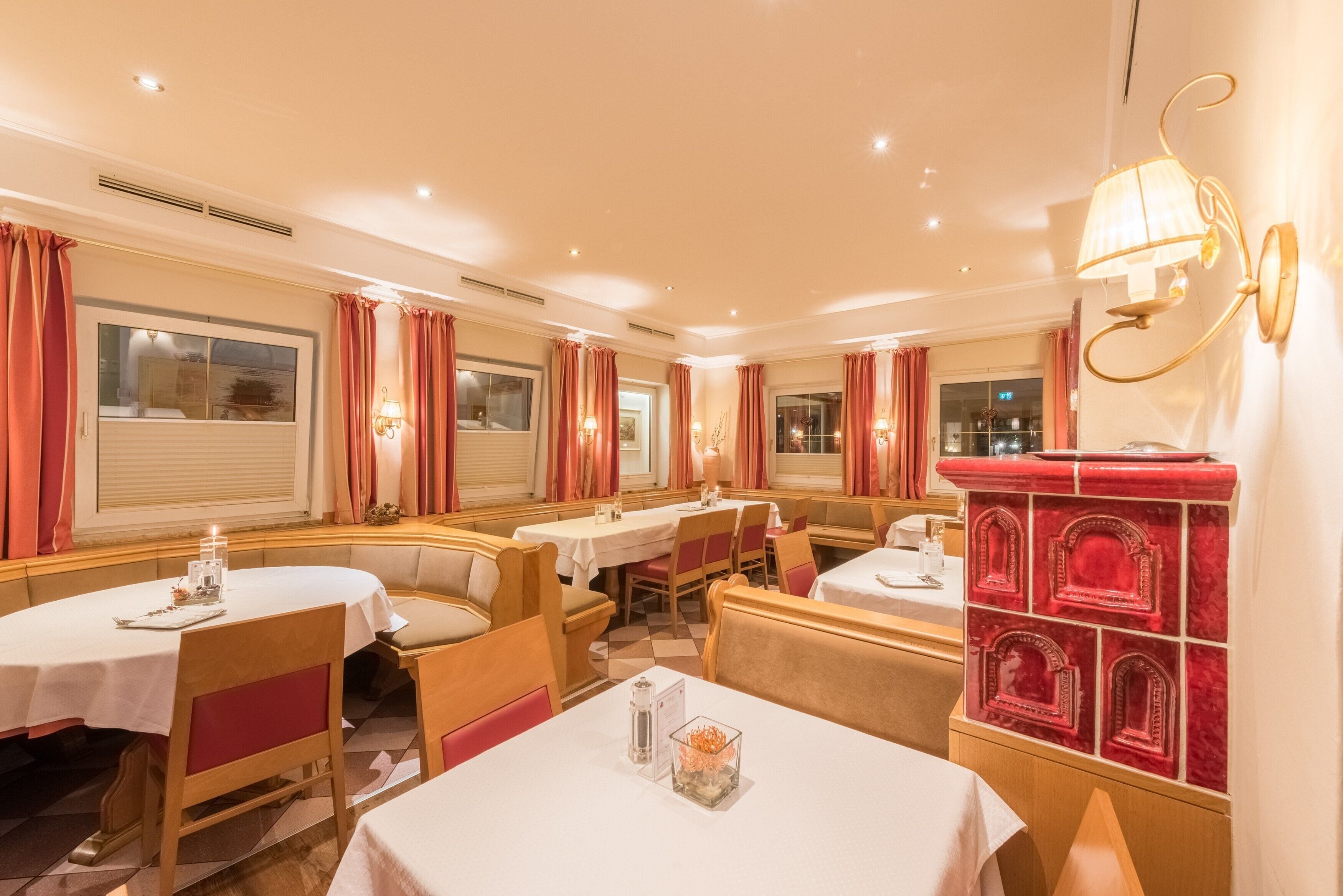 Een restaurant met ronde tafels, gestoffeerde zitjes en rode gordijnen.
