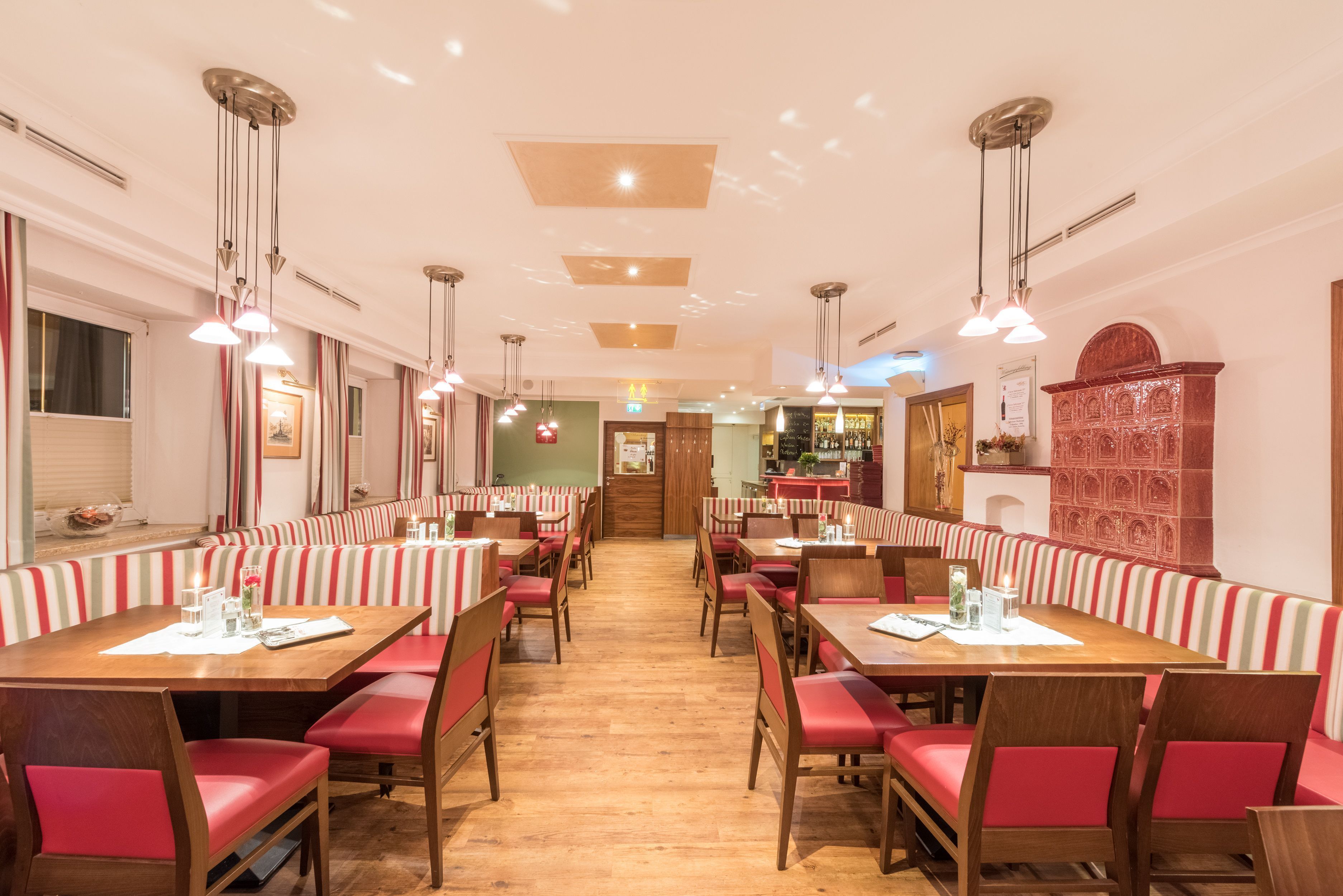 Un restaurante con cabinas y mesas, suelo de madera y lámparas colgantes.