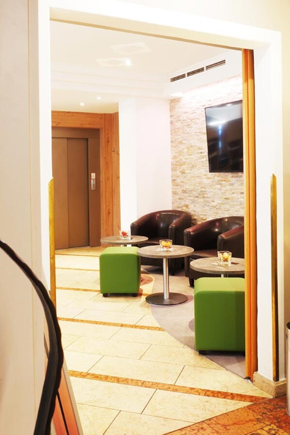 Un hall d’entrée avec des canapés en cuir, des poufs verts et un téléviseur à écran plat fixé au mur.