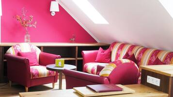 A cozy loft-style living room with a sloped ceiling, wooden flooring, and a mix of red and striped furniture.