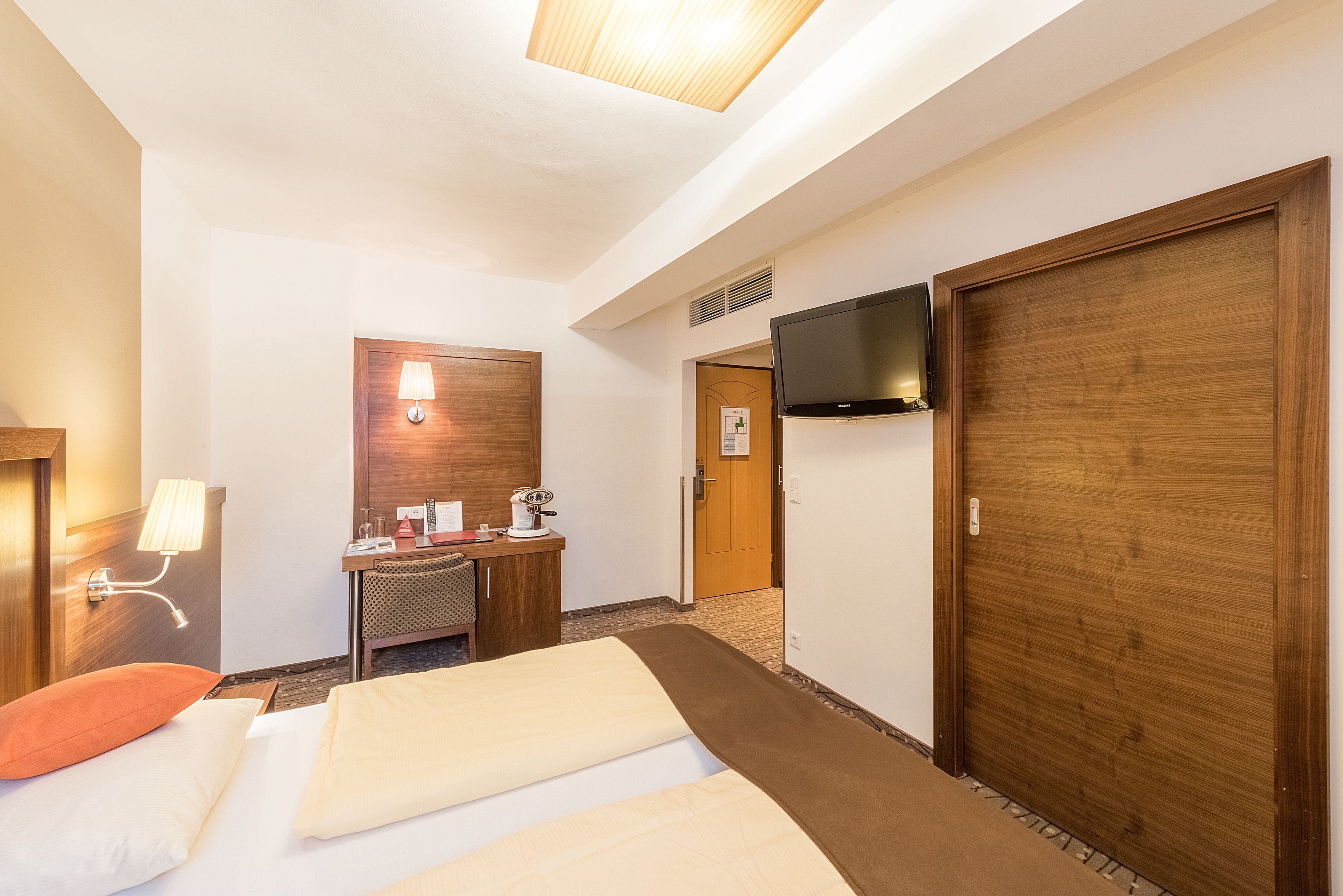 Habitación de hotel con dos camas, un escritorio con lámpara, televisión y una puerta de madera.