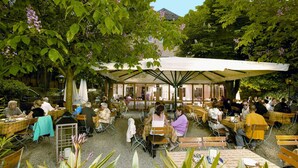 An outdoor café with tables and chairs, surrounded by trees and covered by a canopy.
