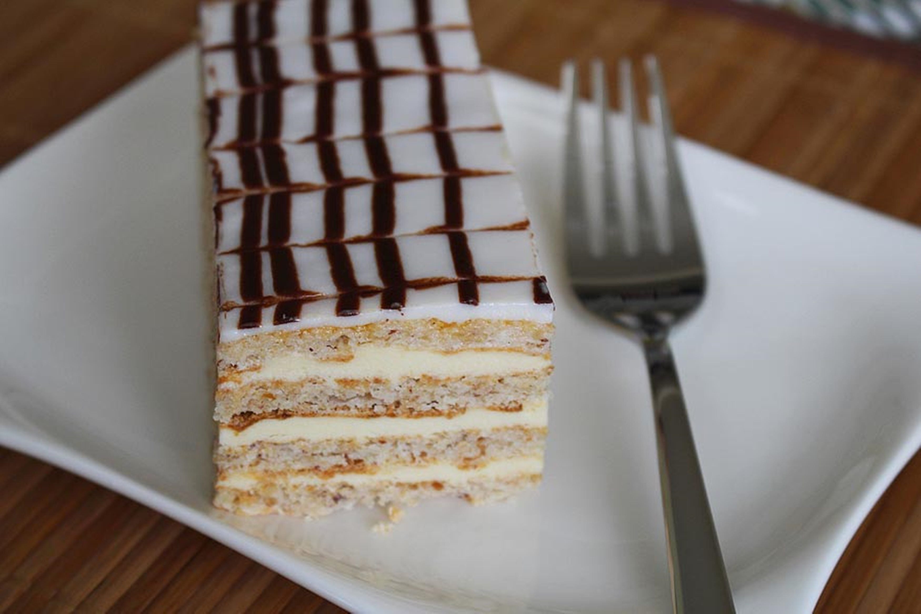 A rectangular cake with white icing and chocolate drizzle on a white plate.