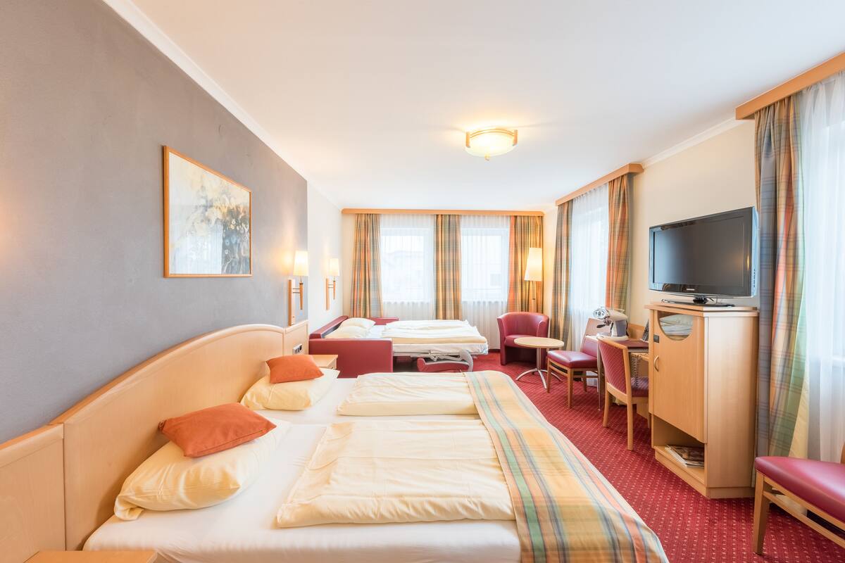 A hotel room with a large bed, a desk, a chair, a television, and a wardrobe.