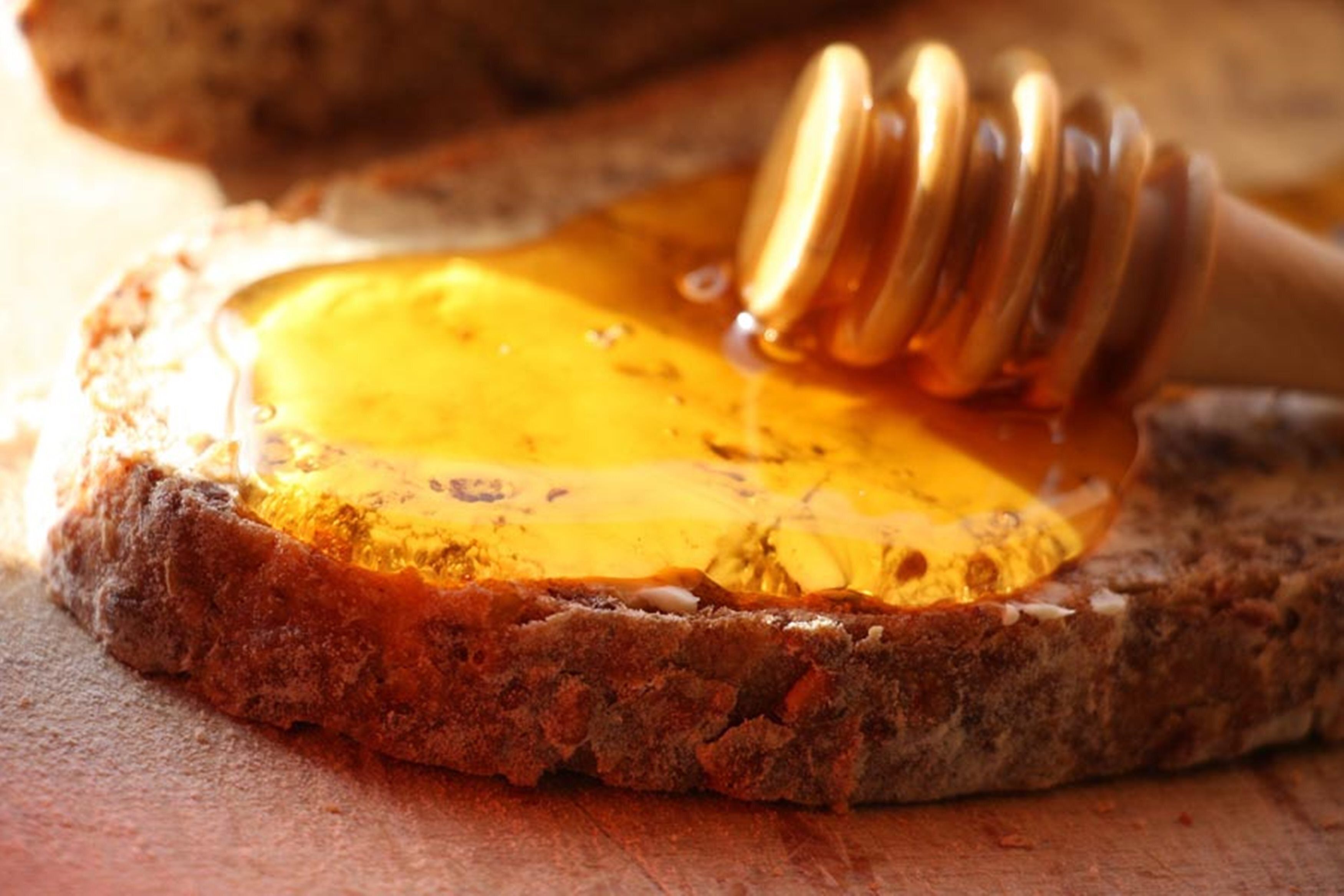 A slice of bread with honey being drizzled on it.
