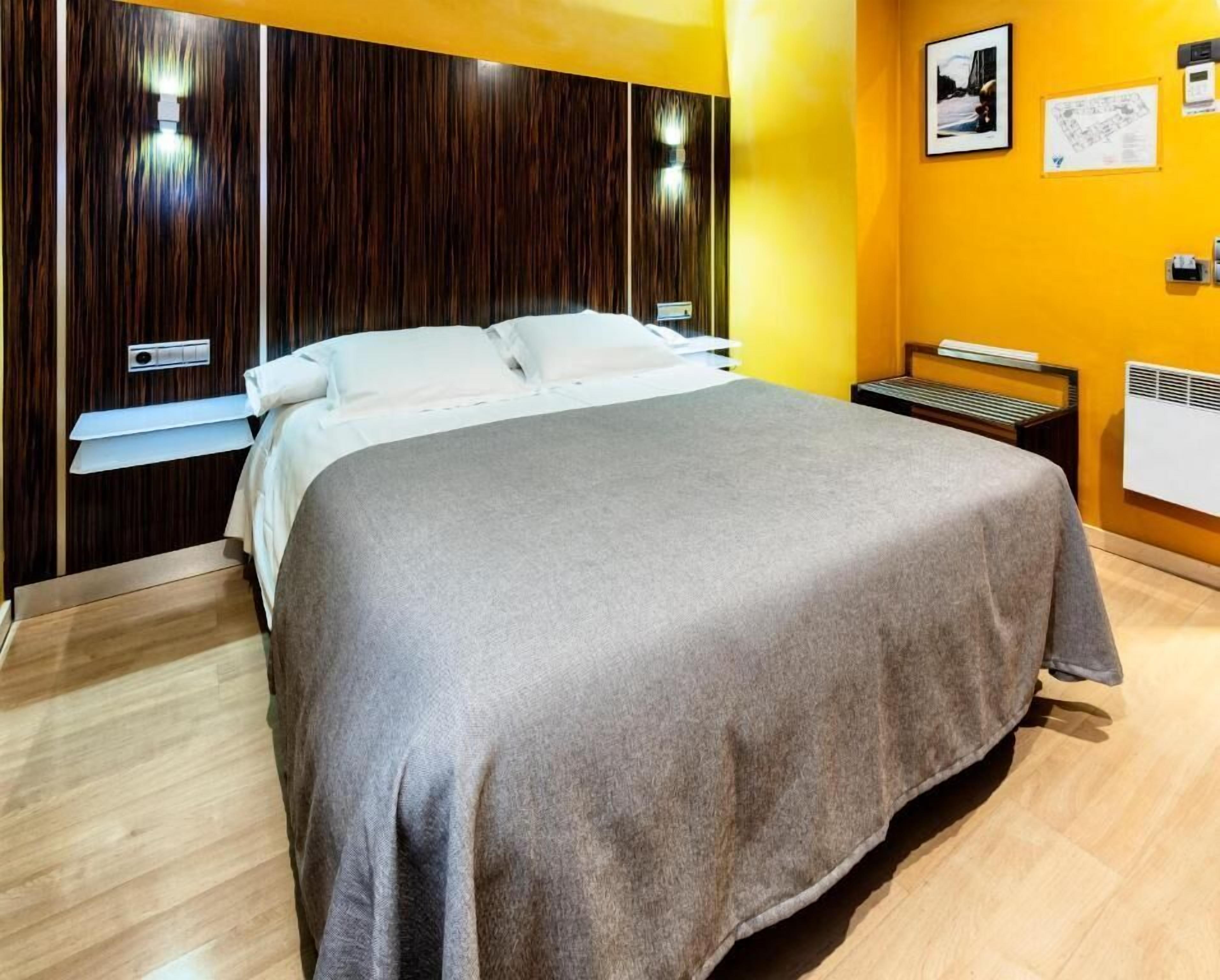 Ein modernes Hotelzimmer mit einem großen Bett, Holzvertäfelung an den Wänden, einem kleinen Nachttisch und einem Wandheizkörper.