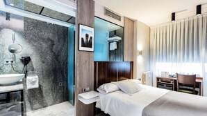 Una habitación de hotel moderna con una cama, una mesita de noche y un baño con lavabo y espejo.