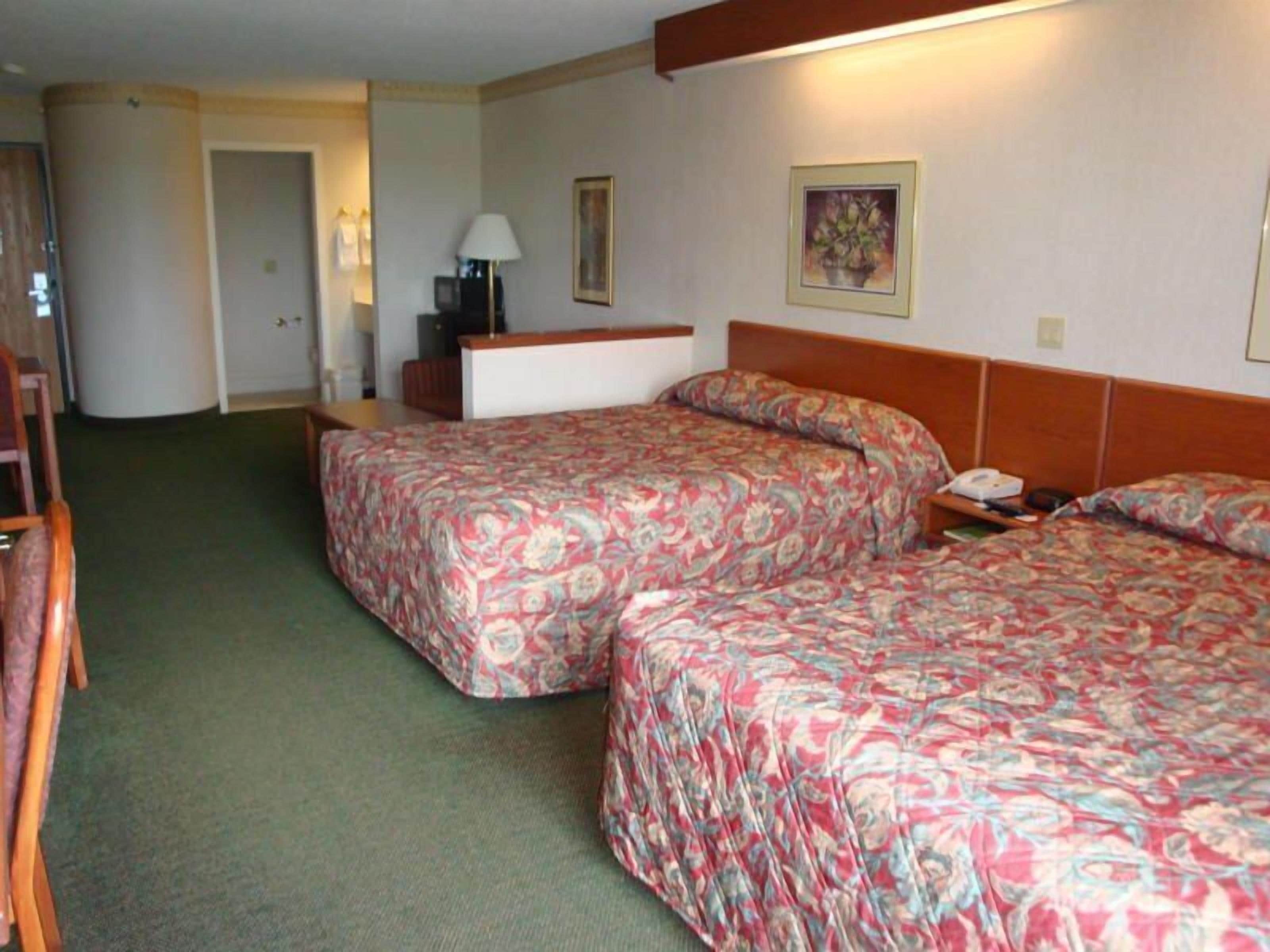 A hotel room with two beds, a desk, a chair, and a lamp.