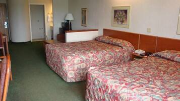 A hotel room with two beds, a desk, a chair, and a lamp.