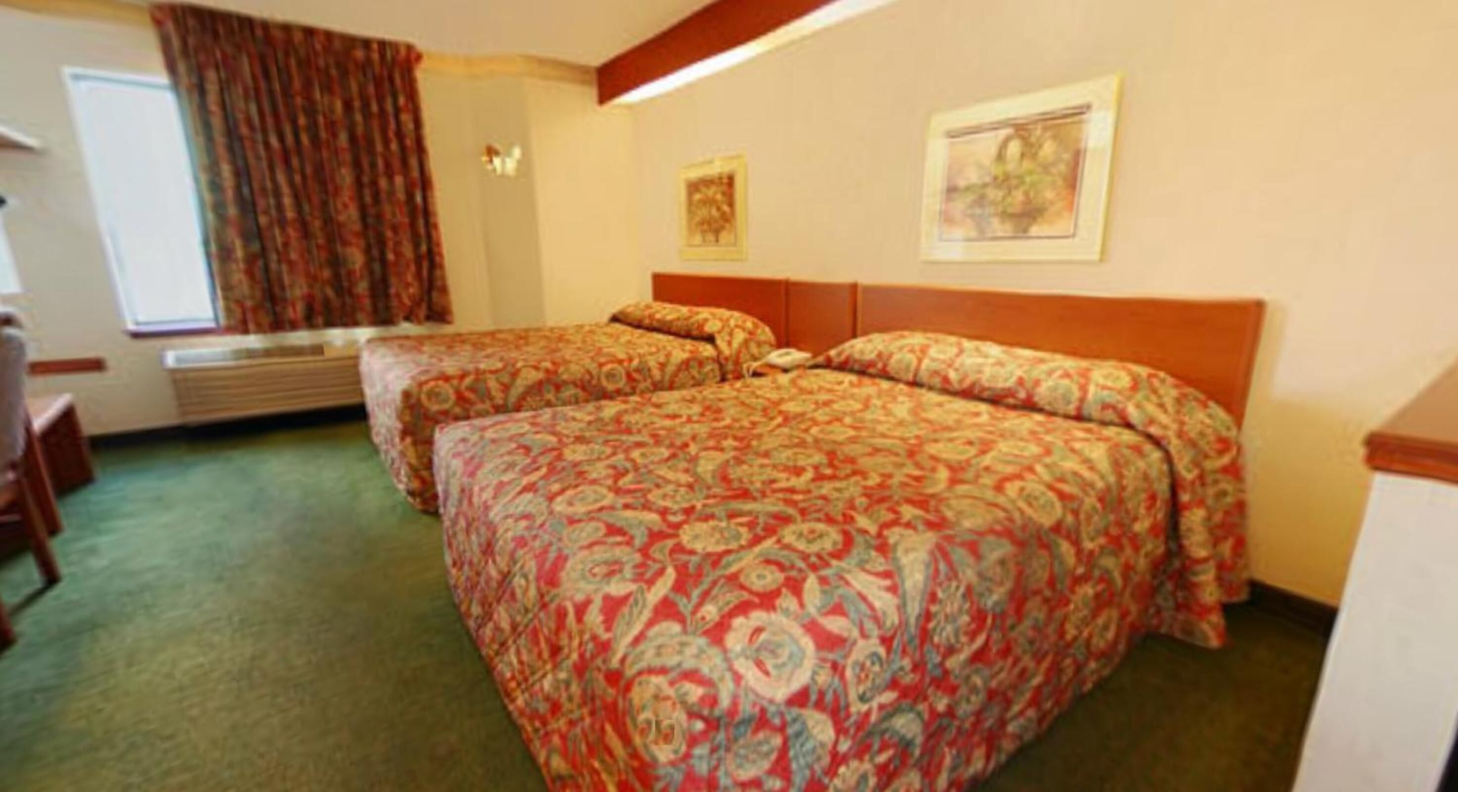 Una habitación de hotel con dos camas, una ventana con cortinas, un radiador y dos cuadros en la pared.