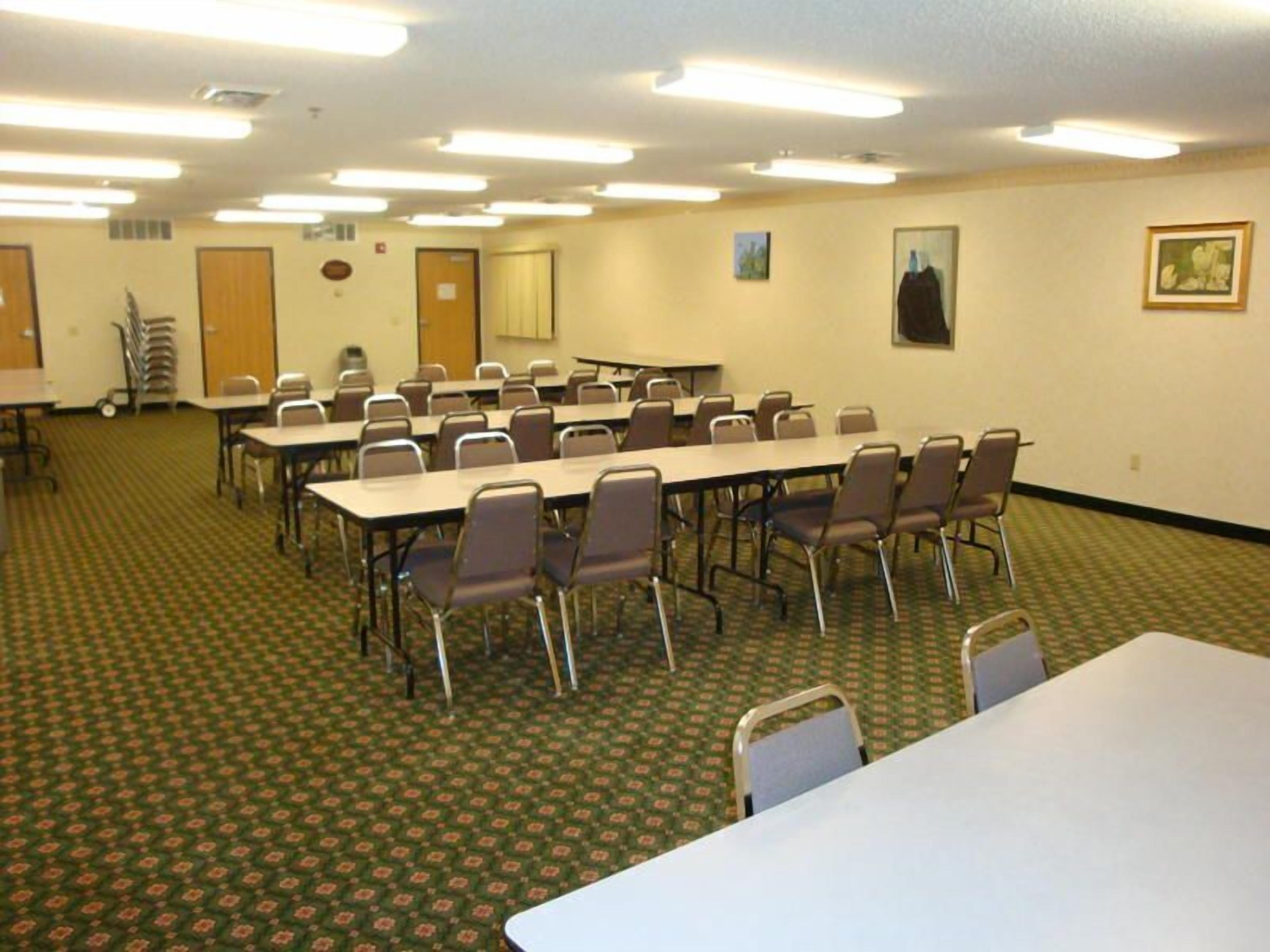 A conference room with multiple tables and chairs, carpeted floor, and ceiling lights.