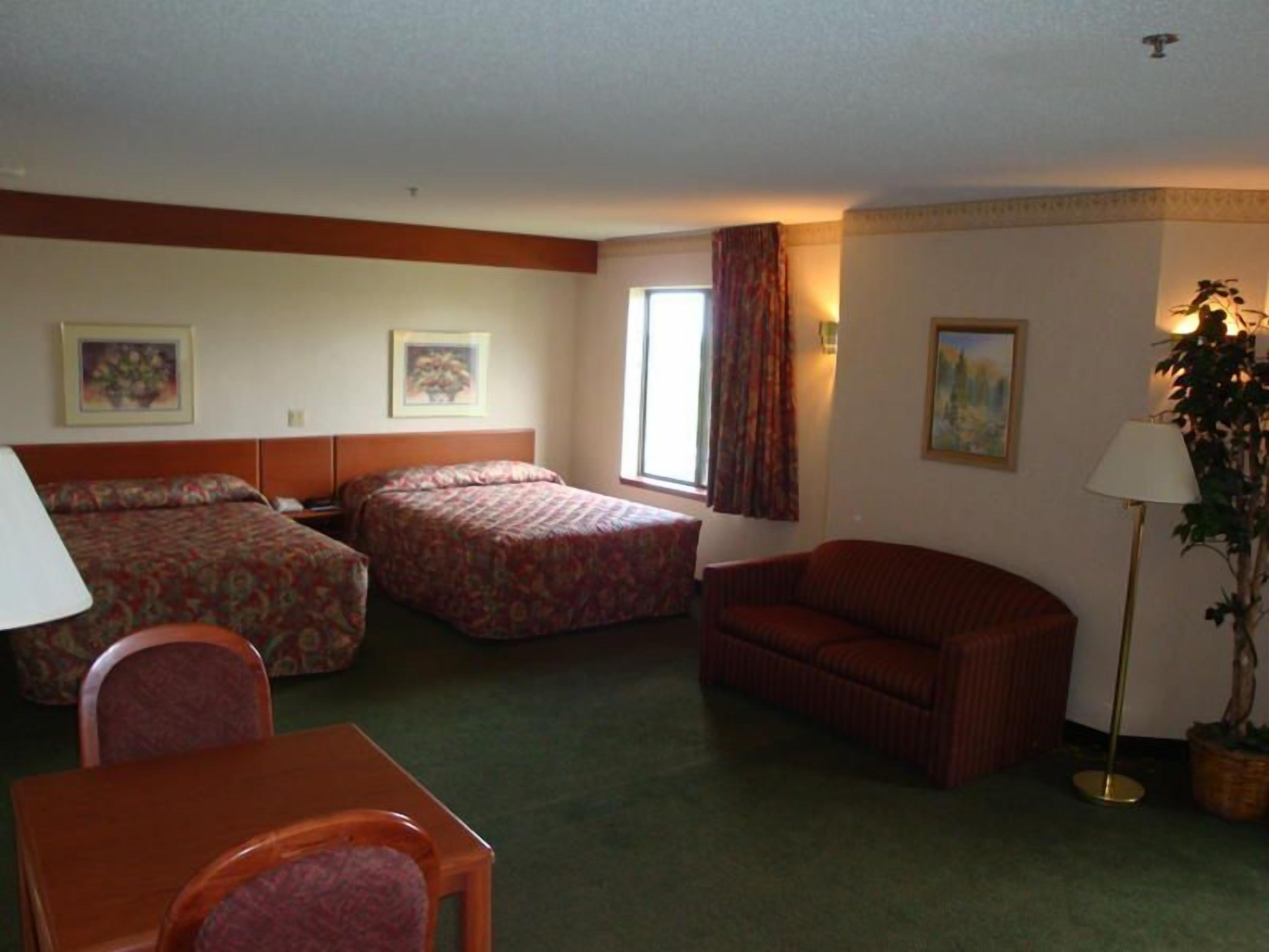 A hotel room with two beds, a sofa, a table, and a chair.