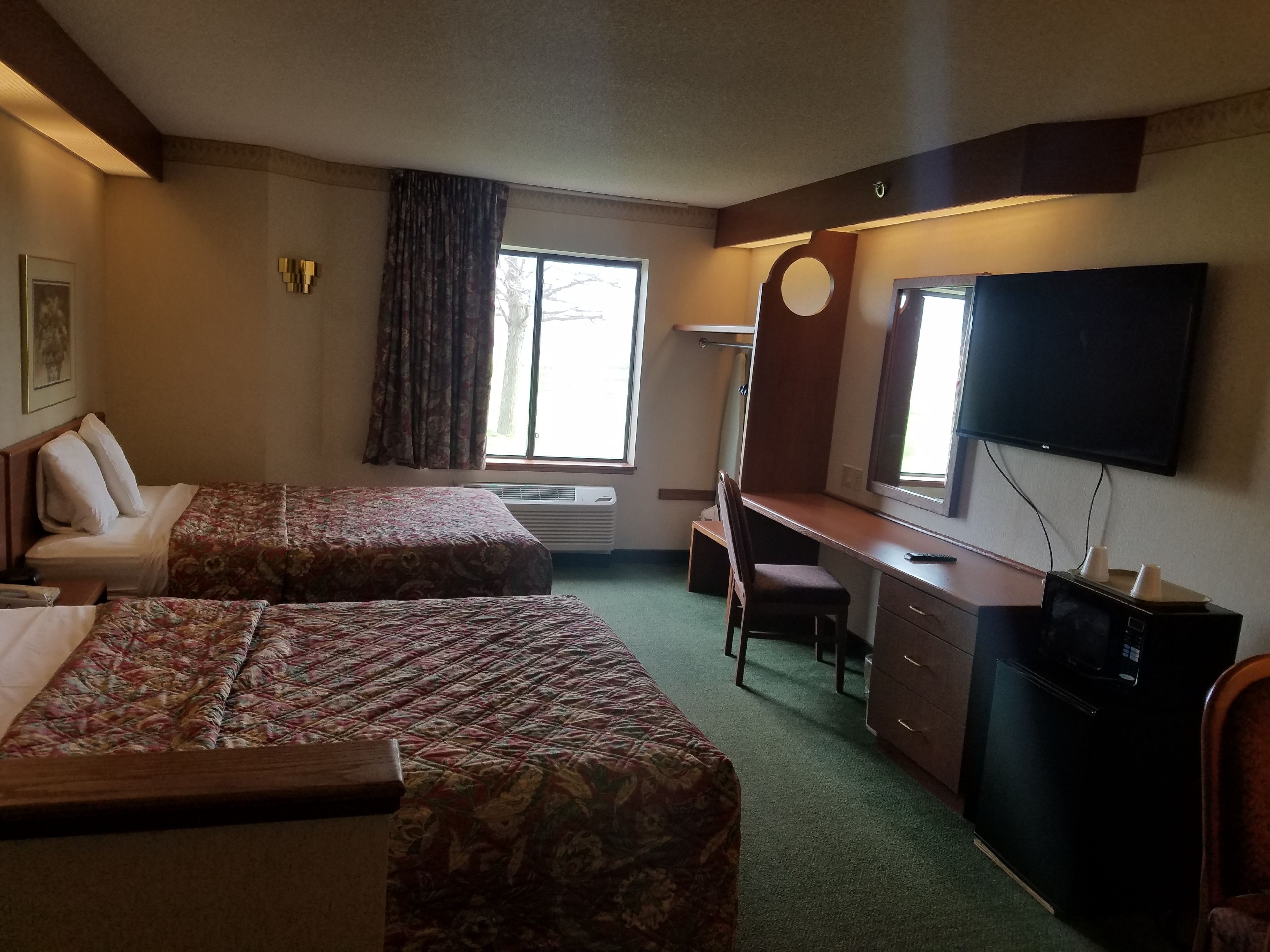 A hotel room with two beds, a desk, a chair, a television, and a refrigerator.