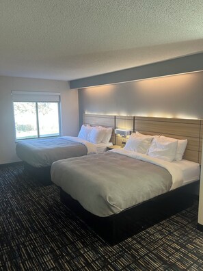 A hotel room with two beds, a large window, and a carpeted floor. - Syracuse Inn & Suites (Syracuse)