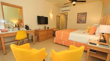 Habitación de hotel con cama, escritorio, sillas, televisor y ventilador de techo.