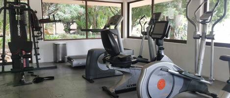 A gym with cardio machines, weight machines, and a large window offering a view of greenery.