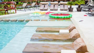A pool with stepping stones, lounge chairs, and a floating ring.