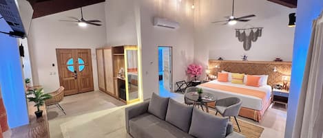 A spacious living area with a grey sofa, a dining table, and a kitchen area visible through an open door.