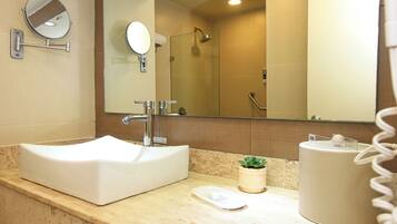 Une salle de bain avec un lavabo blanc, un miroir, une douche et une petite plante en pot.