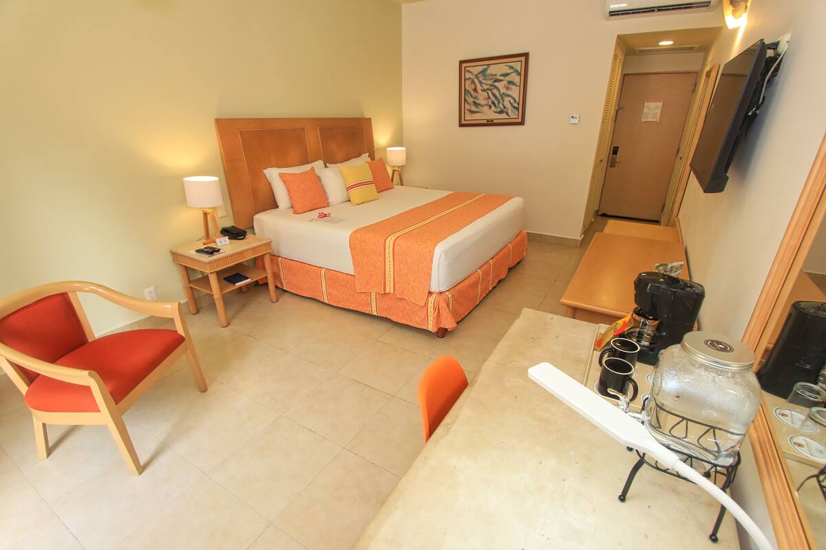 Ein Hotelzimmer mit Bett, Sessel, kleinem Tisch und Kaffeemaschine.