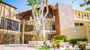 A modern building with a glass facade, a wooden structure with a thatched roof, and a sign reading "NIRU BEACH CLUB".