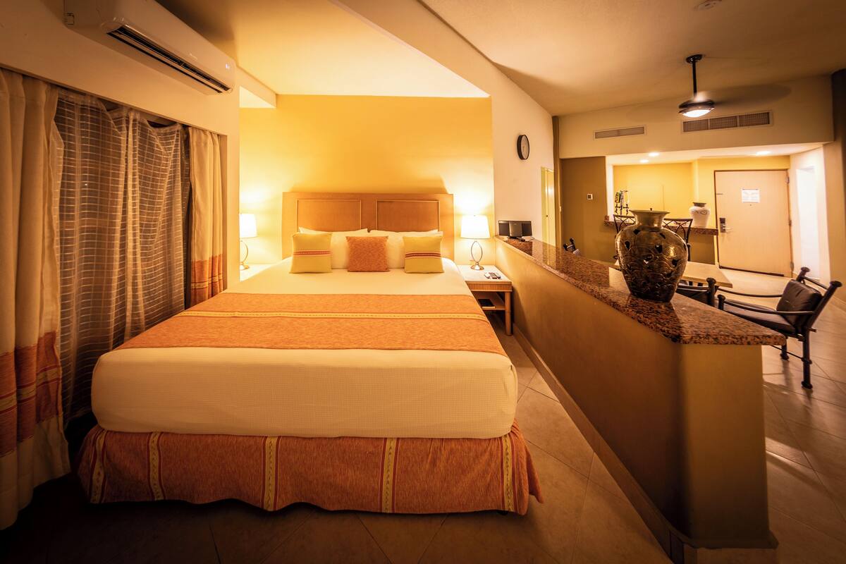 Ein Hotelzimmer mit einem großen Bett, einem Schreibtisch, einem Sessel, einer Vase und einer Wanduhr.