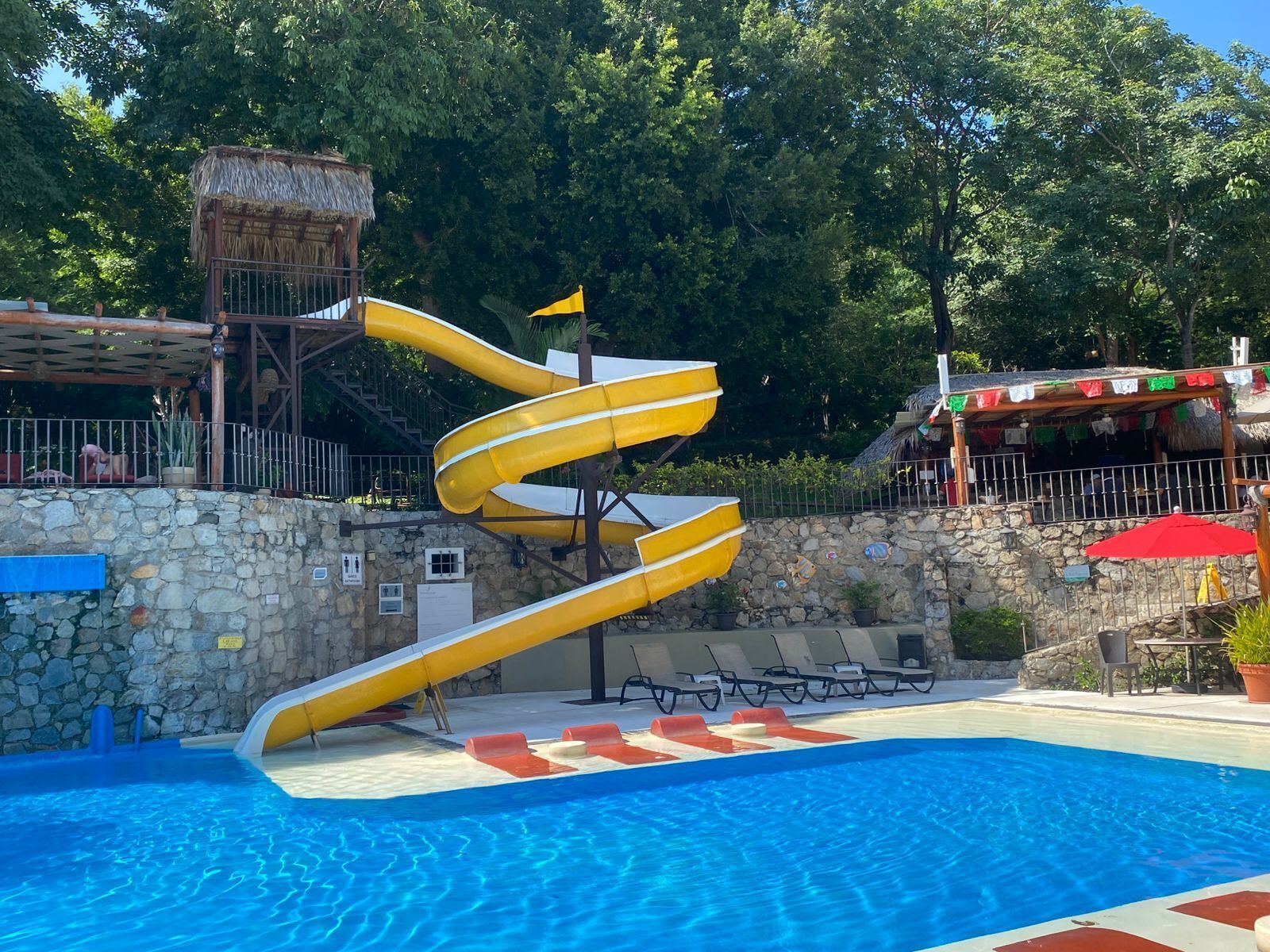 Una piscina con un tobogán en espiral amarillo y una estructura de techo de paja.