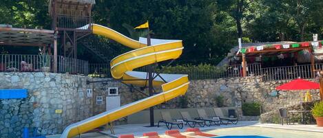 Una piscina con un tobogán en espiral amarillo y una estructura de techo de paja.