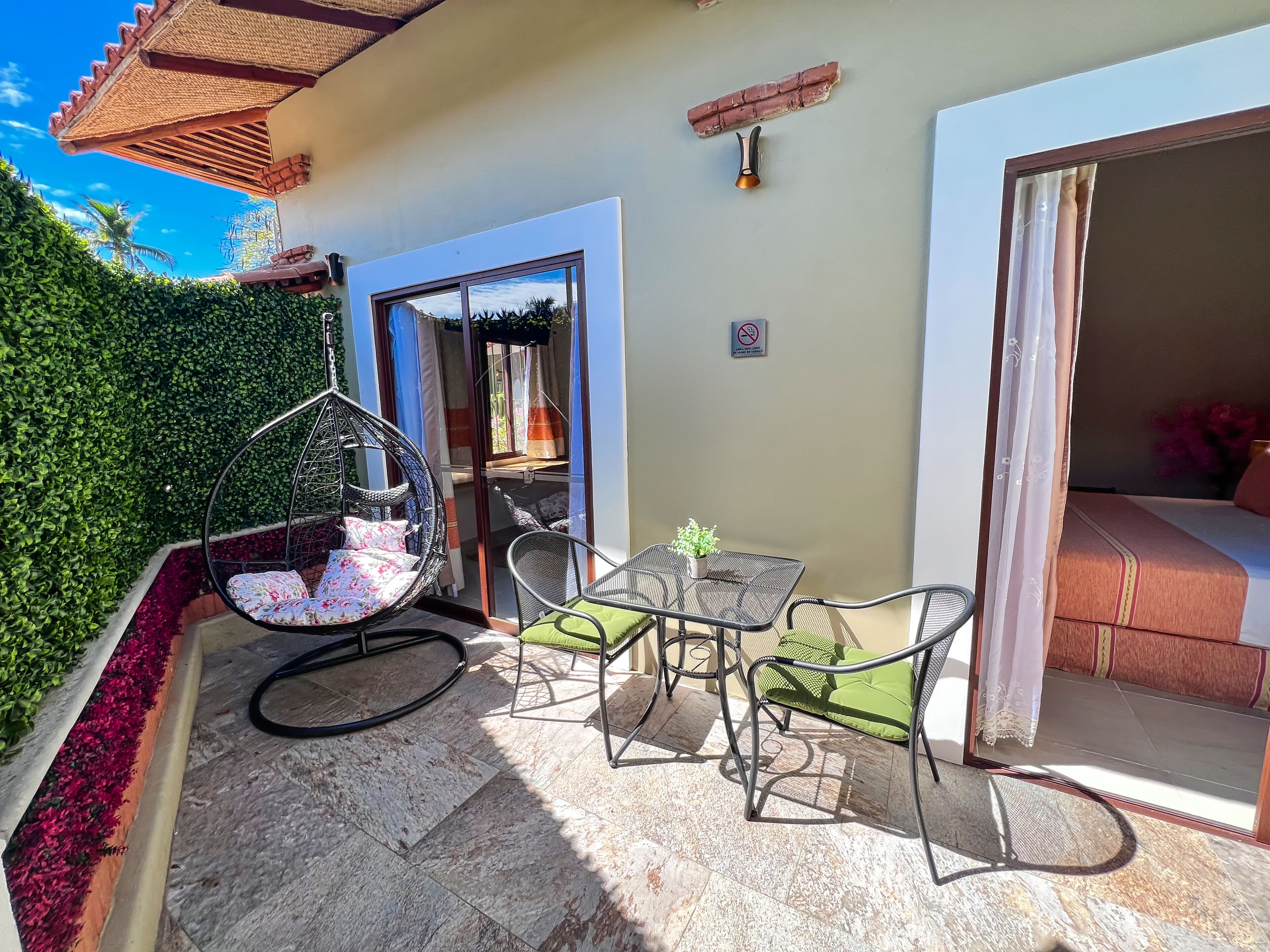 A patio with a hanging chair, a table with a potted plant, and a bed with a curtain.
