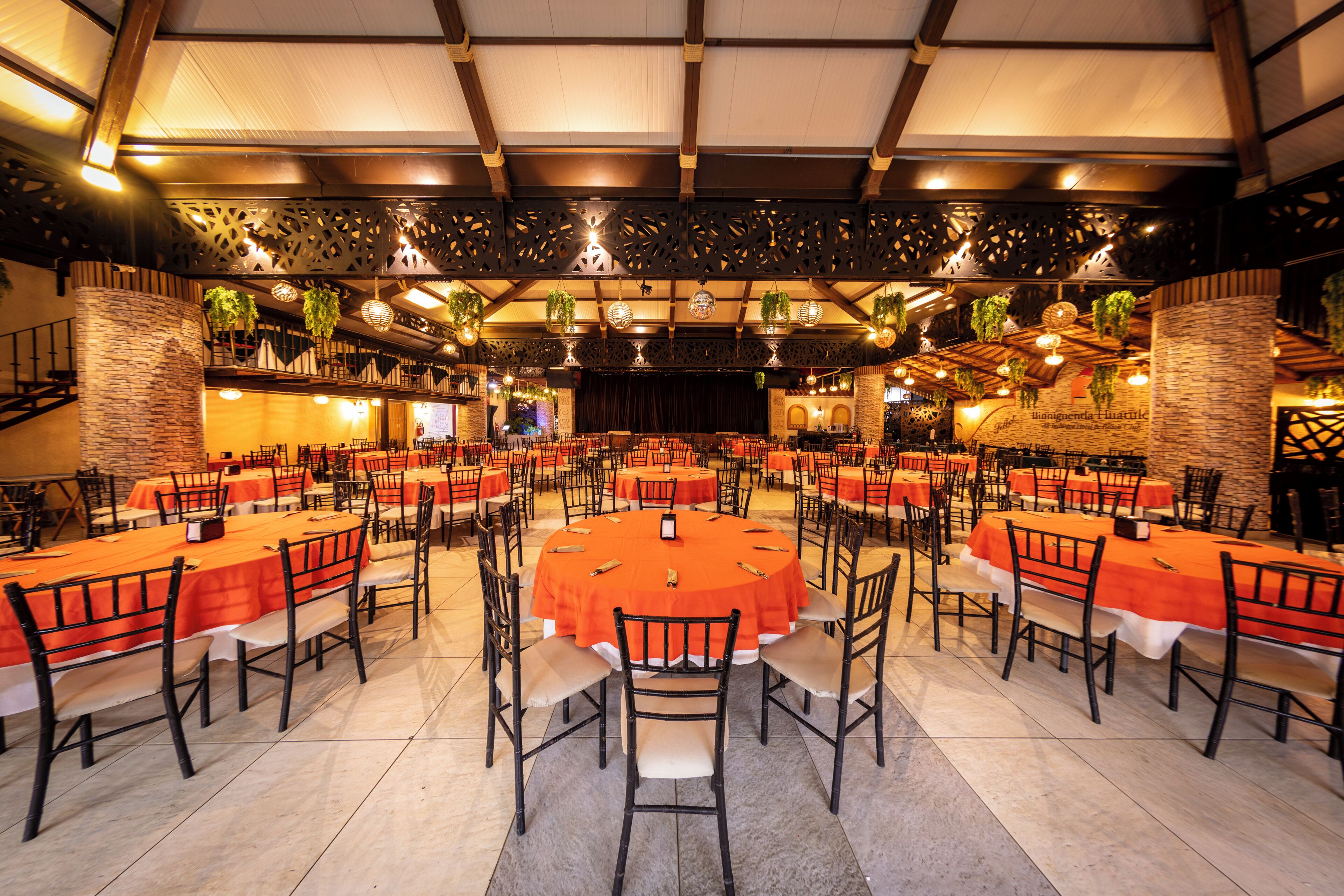 Un salón de banquetes con varias mesas redondas, sillas y un escenario.