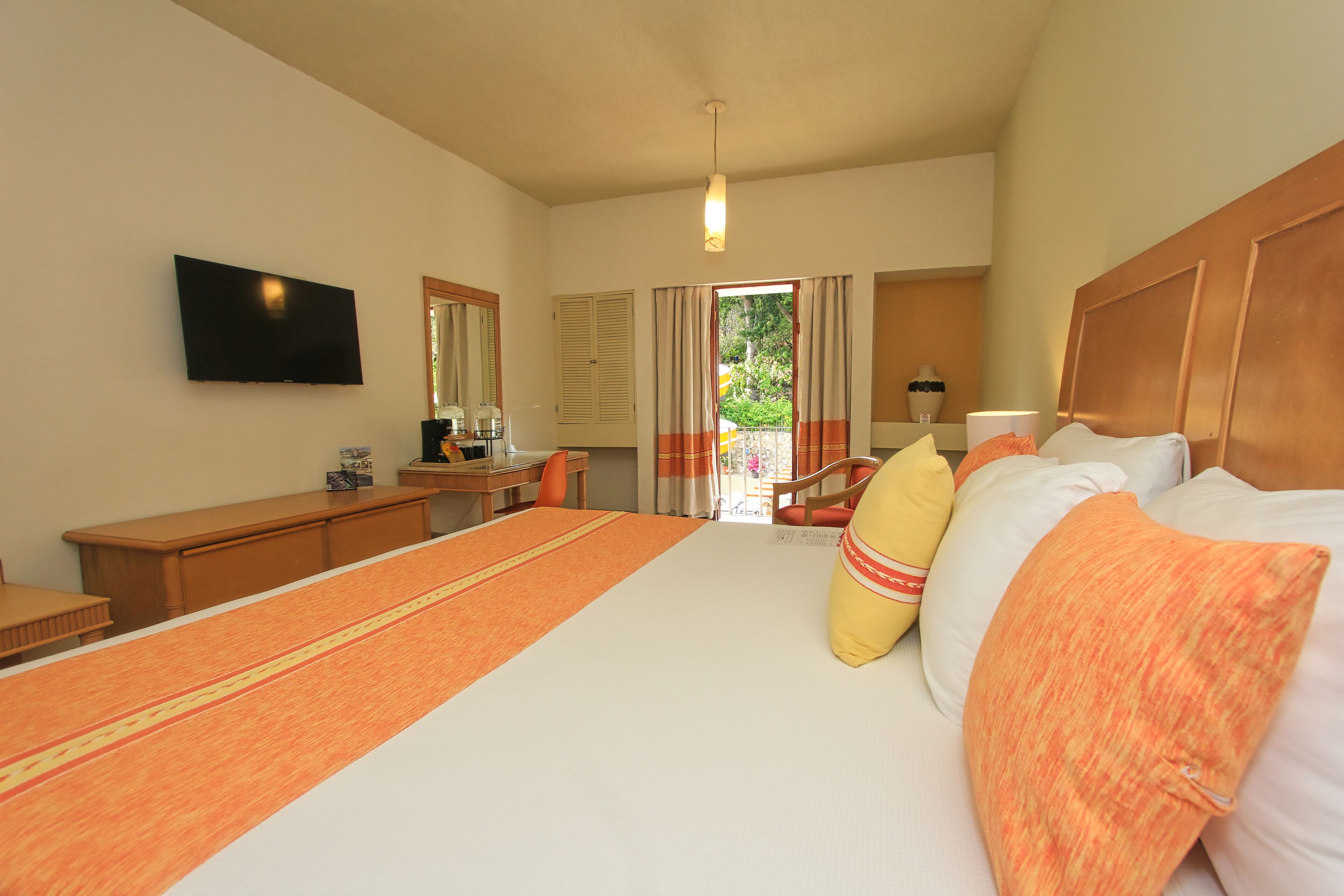 Une chambre d’hôtel avec un grand lit, un bureau, une chaise, une télévision et une fenêtre avec des rideaux.