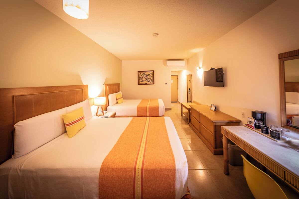 Ein Hotelzimmer mit zwei Betten, einem Schreibtisch, einem Stuhl, einem Fernseher und einem sichtbaren Badezimmer im Hintergrund.