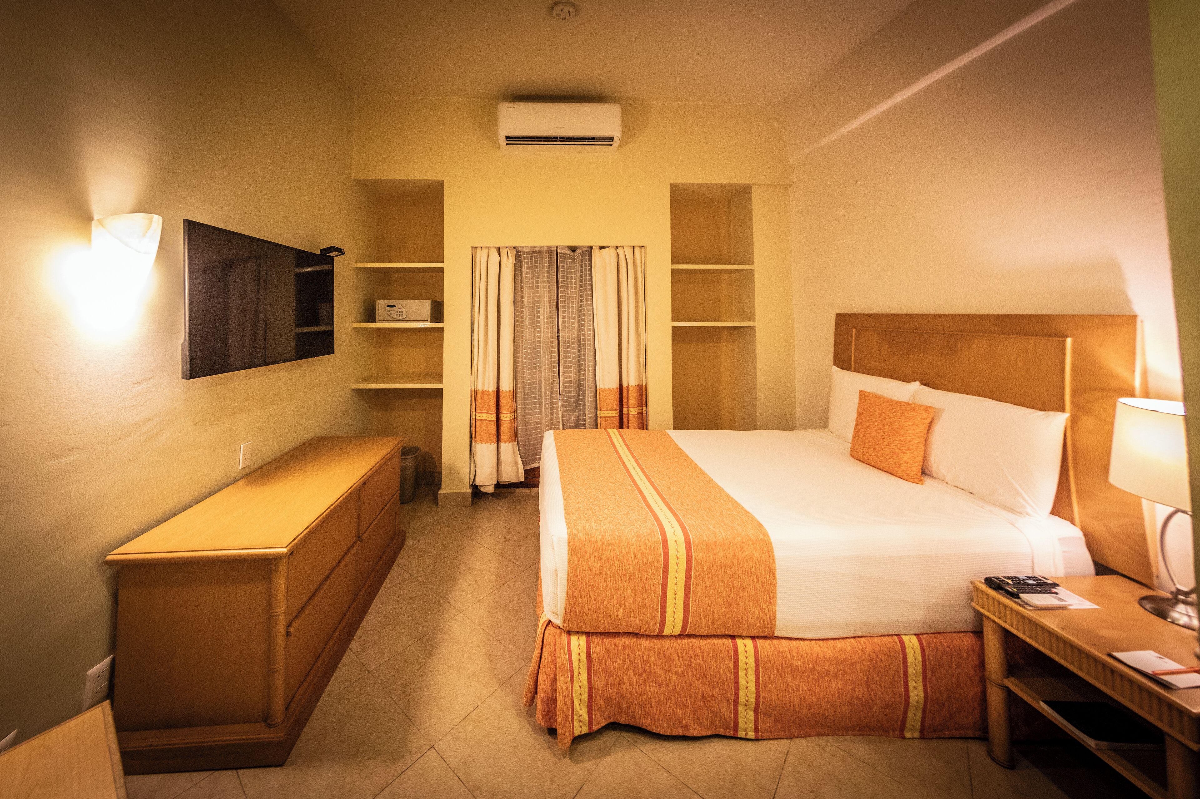 Habitación de hotel con cama, escritorio, televisor y estantería.