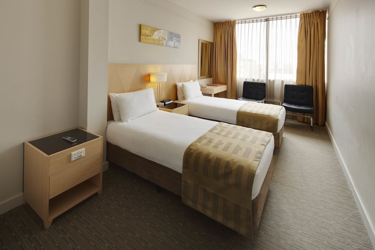 A hotel room with two beds, a desk, a TV, and a window with curtains.