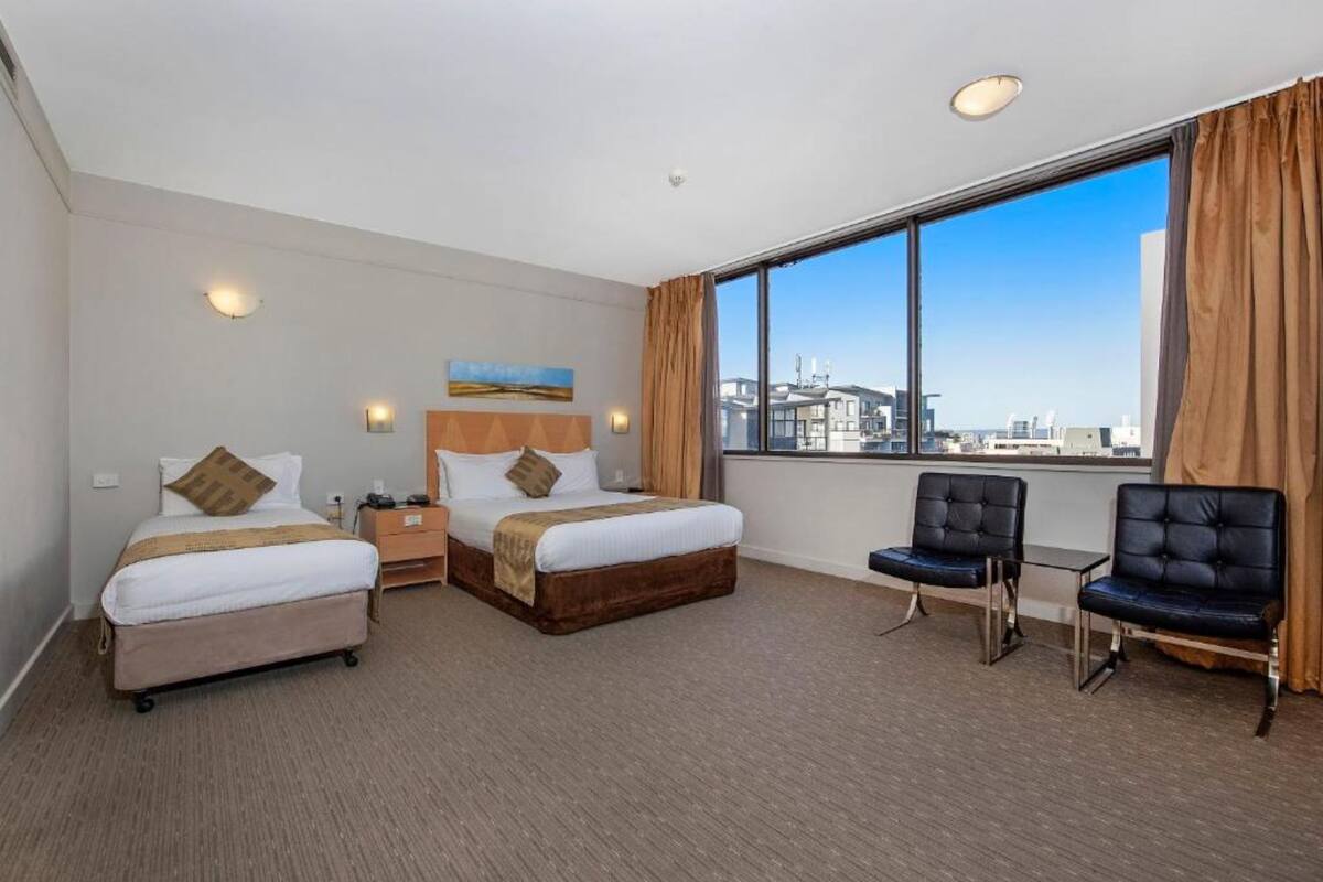 A hotel room with two beds, a desk, a chair, and a large window with a city view.
