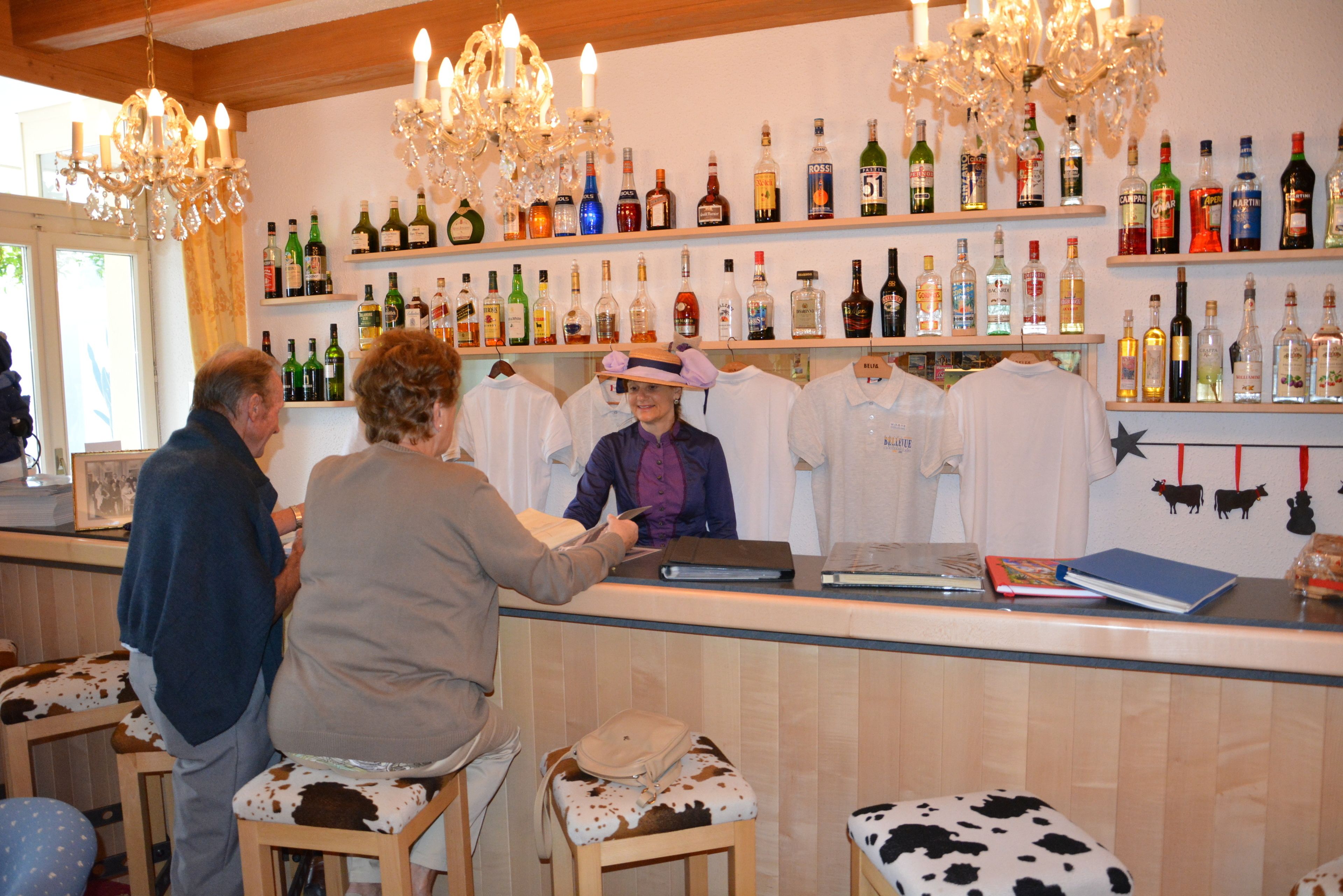 A bar area with a variety of liquor bottles on shelves, a counter with a person behind it, and cow-print stools.