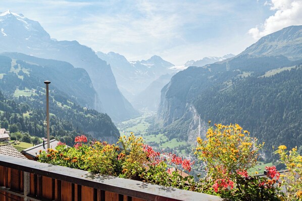 A scenic view of a valley with mountains, a wooden balcony with flowers, and a street lamp.