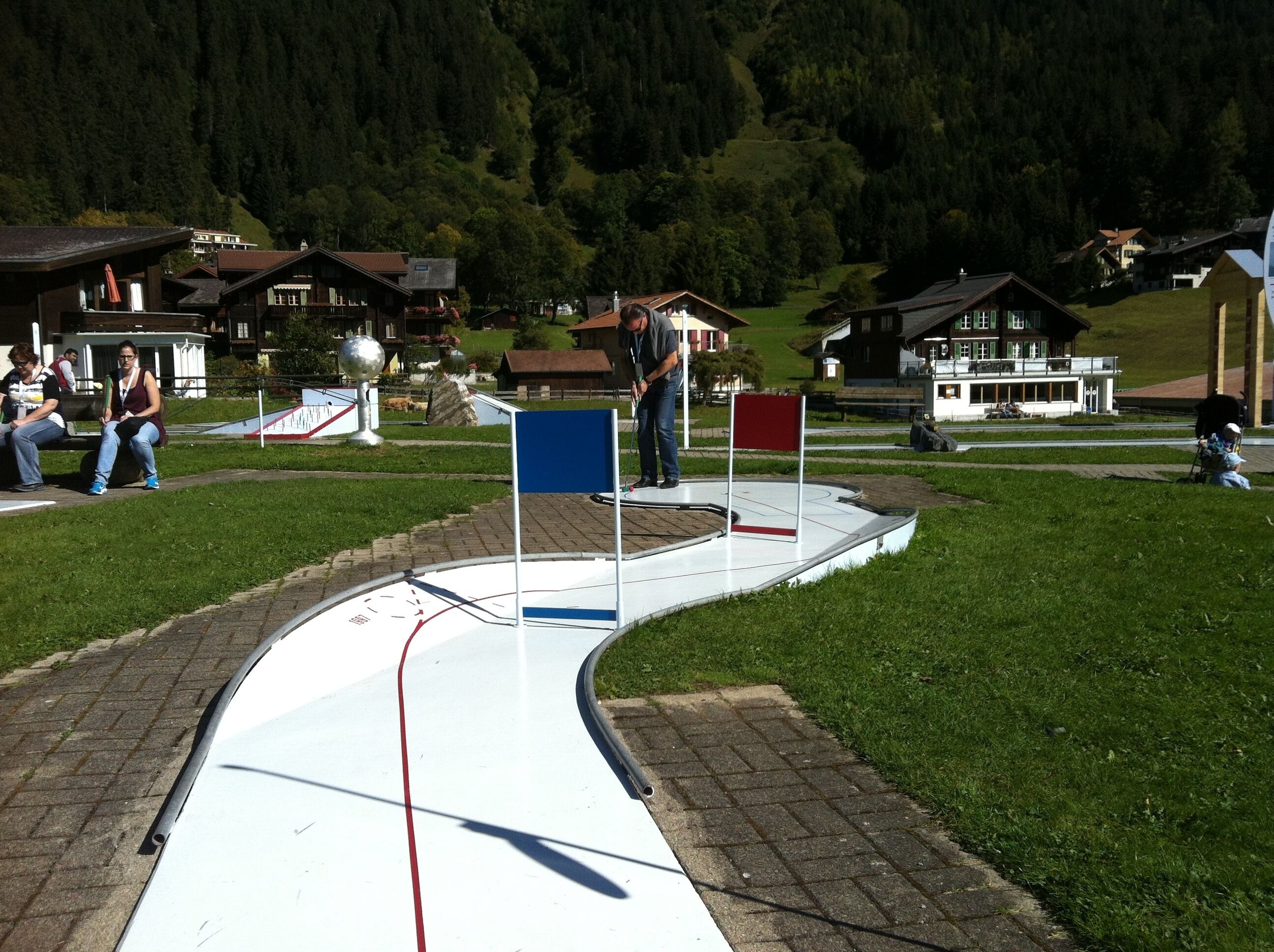 A ski slope with a red and blue sign, surrounded by houses and a forested hill.