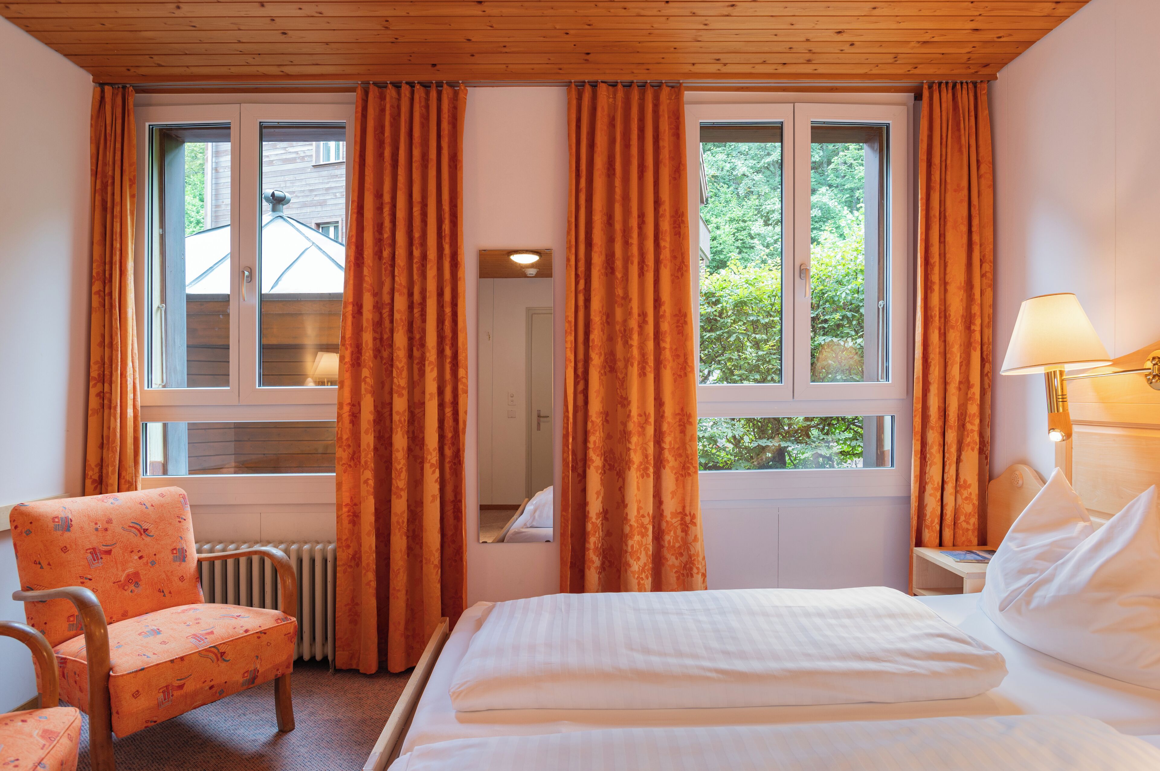 Una habitación de hotel con cama, una silla, una mesita de noche y una ventana con cortinas.