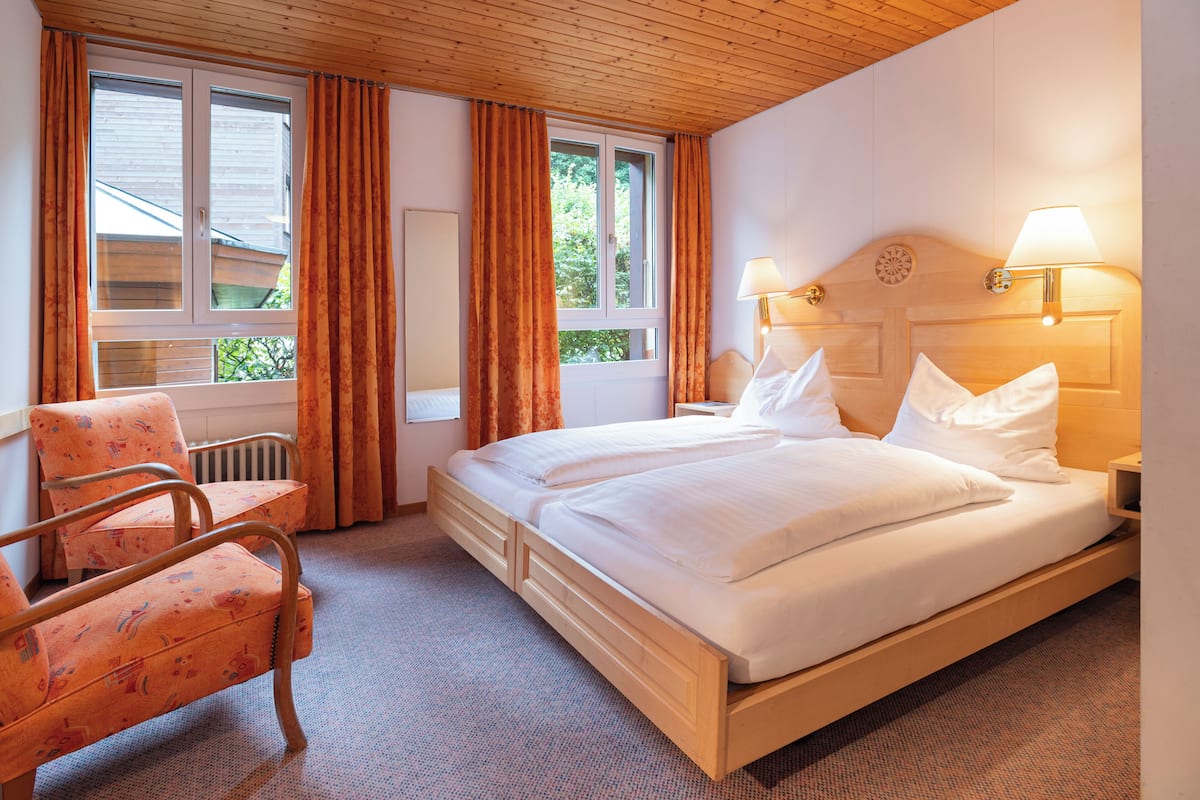 Ein Hotelzimmer mit einem hölzernen Bett, zwei Nachttischlampen, einem Sessel und einem Fenster mit Vorhängen.