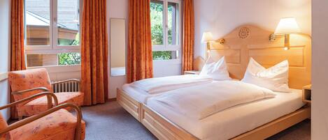 Une chambre d’hôtel avec un lit en bois, deux lampes de chevet, une chaise et une fenêtre avec des rideaux.