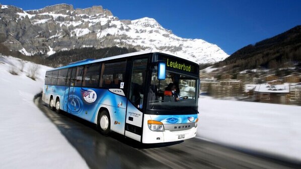 A bus with "Leukerbad" written on the front, traveling on a snowy road with mountains in the background. - Le Bristol Leukerbad (Leukerbad)