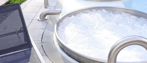 Un área de piscina con tres jacuzzis, una tumbona y una mesa con vasos y una botella.