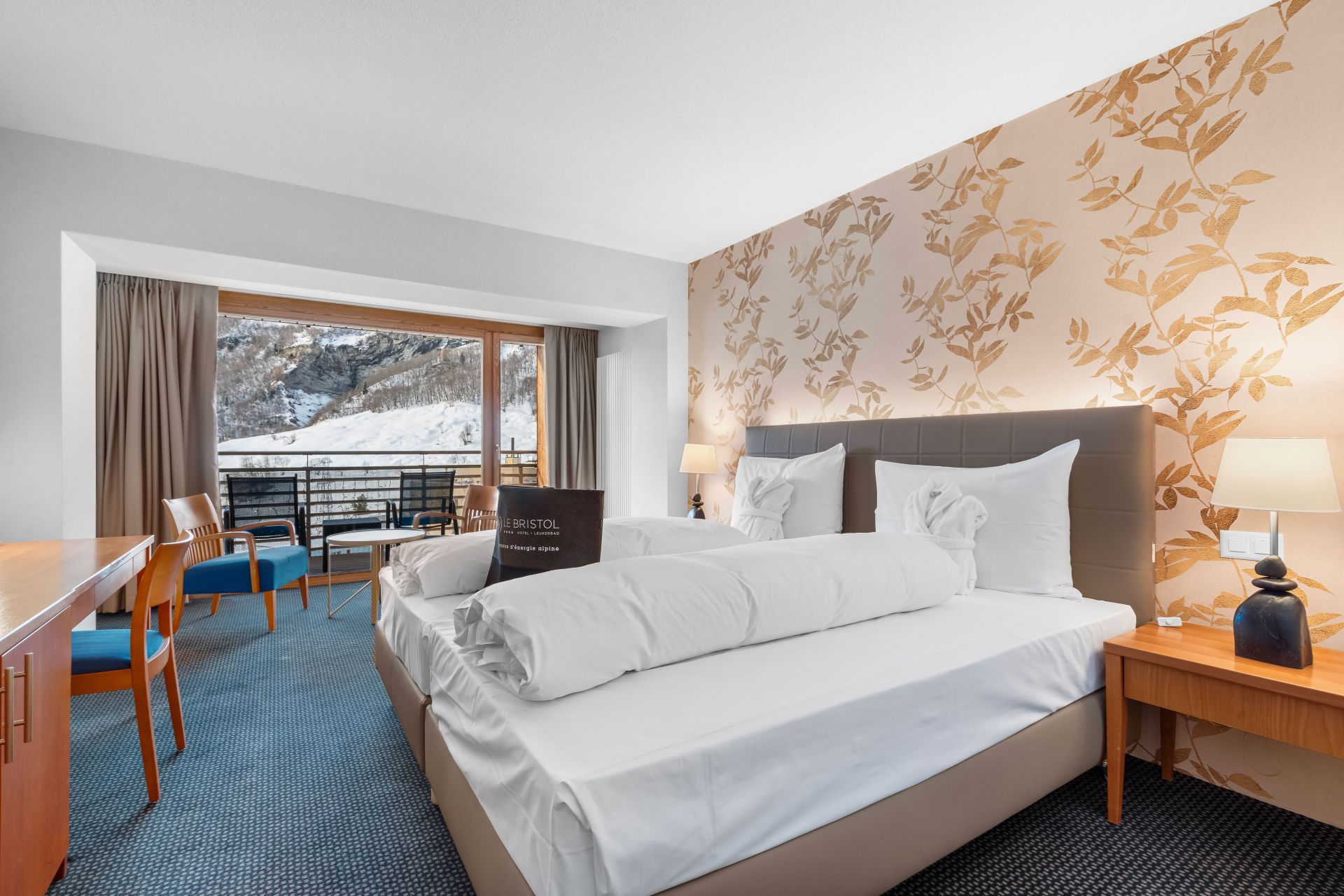 A hotel room with a bed, a desk, and a chair. There is a view of a snowy landscape through large windows.