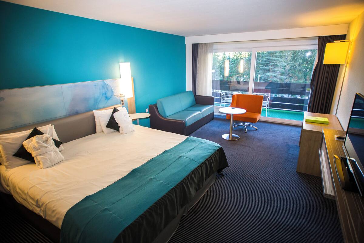 A hotel room with a bed, a sofa, a small table, and a TV.
