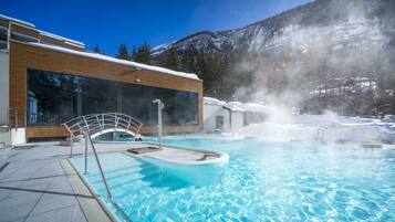 Ein Pool mit Glasüberdachung und ein Whirlpool, umgeben von Schnee und Bäumen.