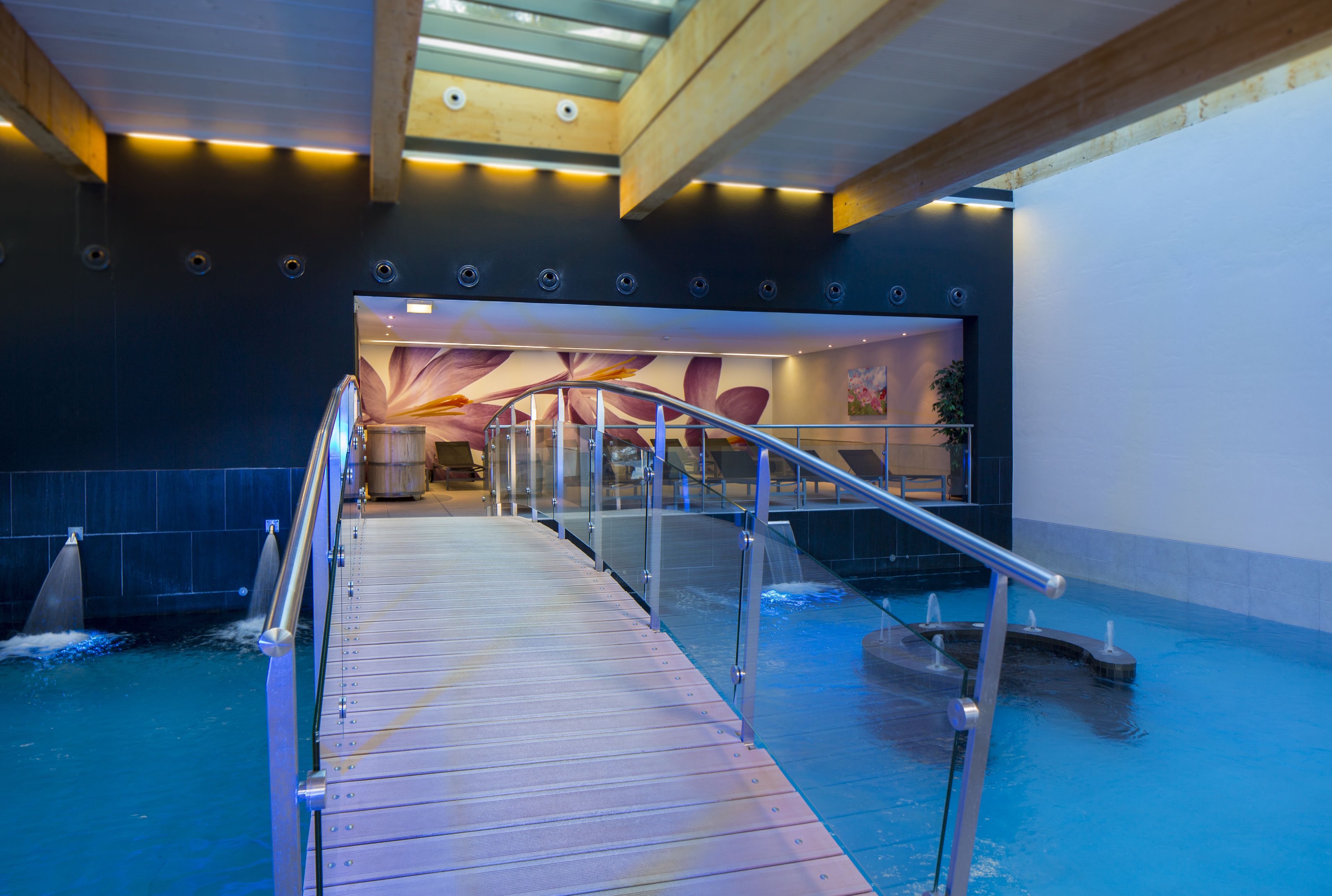 An indoor swimming pool with a wooden deck and metal railings.