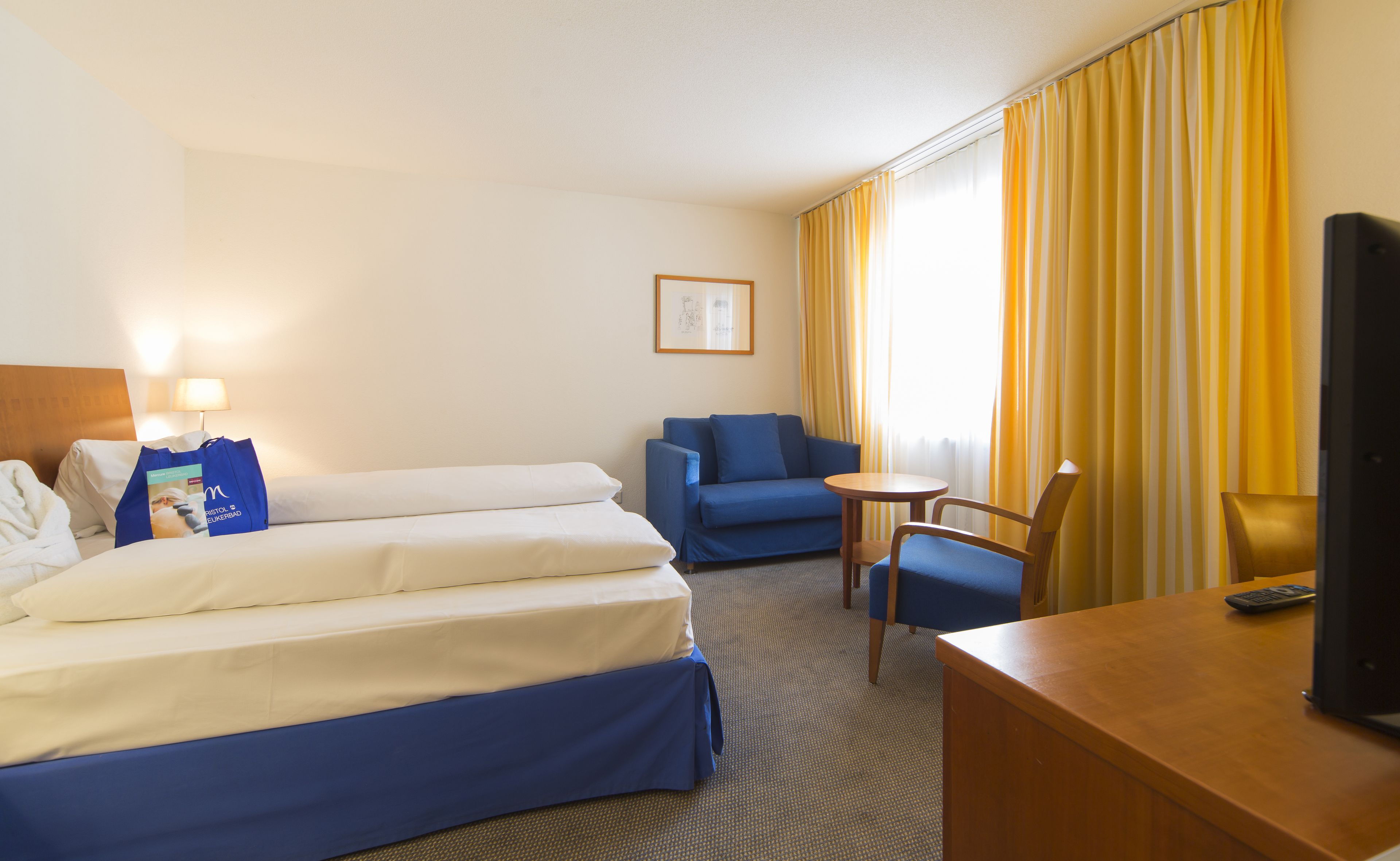 Una habitación de hotel con una cama, un sofá azul, una mesita pequeña y un escritorio con un ordenador.
