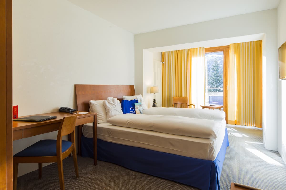 A hotel room with a bed, a desk, a chair, a TV, and a window with curtains.