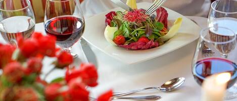A dining table with a white plate of food, wine glasses, and cutlery.